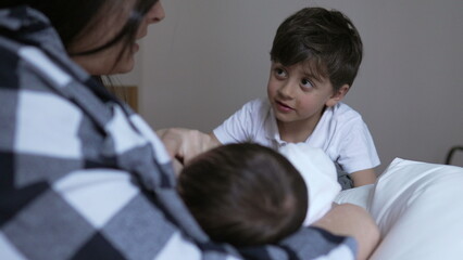 Obraz premium Young boy curiously watching his mother breastfeed his newborn sibling. mother wearing a plaid shirt, holds the baby lovingly while the boy looks on, capturing a moment of family bonding and curiosity