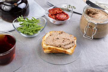 Chicken liver pate with wheat bread, arugula, sun-dried tomatoes and black tea. Homemade traditional rustic cuisine. Breakfast or snack option. Selective focus, close-up.