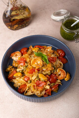 Noodles with shrimps, mussels, tomatoes, onions and capers. Pasta is served with olive oil and pesto sauce. Homemade traditional Mediterranean cuisine. Selective focus, close-up.