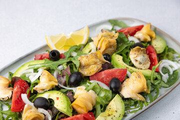 Warm salad with rapans (snails), tomatoes, avocado, arugula, black olives, onions and olive oil. Traditional seafood salad. Close-up, selective focus.