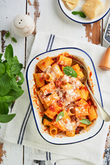 Pasta Rigatoni with parmesan cheese, tomato passata sauce and basil in retro plate on old wooden red  rustic table background. Traditional Italian pasta recipe. Cover or article. Top view.