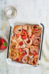 Strawberry rollies puff pastry with custard inside and sprinkled with powdered sugar on white wooden rustic table. Summer breakfast recipe idea. Cover or article. Top view.