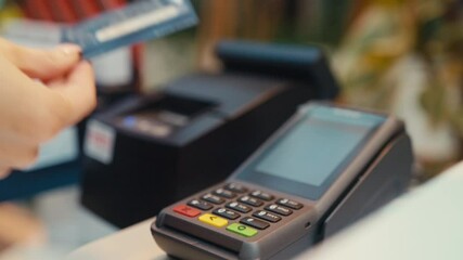 Close-up of a Female Hand Paying with Contactless Credit Card. Customer Doing Transaction with POS terminal in a store. NFC Payment. Wireless Money Transaction.