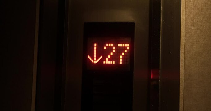 Close-up of an electronic board in an elevator with a floor countdown and red numbers. Go down the elevator, the arrow on the board blinks and shows the direction down.