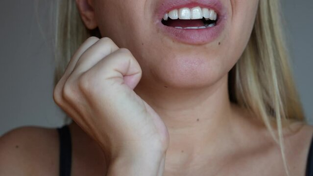 Young caucasian blonde woman with a toothache holding her lower jaw with her hand on dark grey background. The girl suffering from a severe tooth pain. The reaction of sensitive teeth to hot and cold