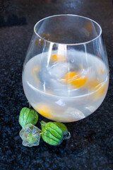 Swirling Gin and tonic with bright orange Gooseberries in it.