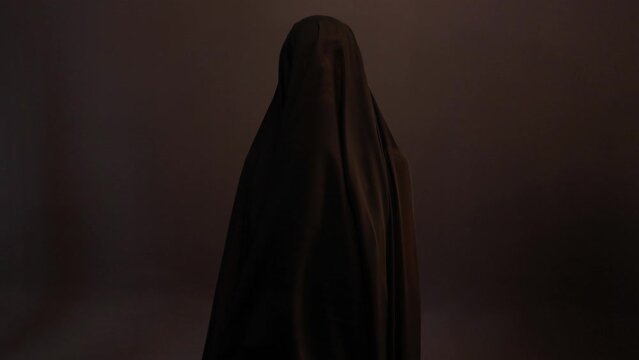 a mystical priestess under a black veil, a woman in black on a dark background, the wind sways the fabric on her face