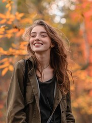 Satisfied woman in casual clothes, standing against a backdrop of a colorful autumn forest, her cheerful smile blending with the warm, seasonal hues