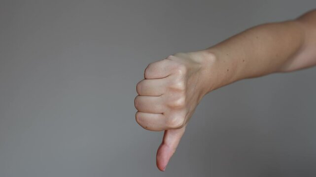 Young woman showing two different signs: thumbs up gesture changing to thumb down gesture, like and dislike on a dark grey background