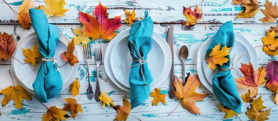 A fall themed table setting featuring vibrant leaves a teal napkin and silverware on a white shiplap board ideal for a copy space image