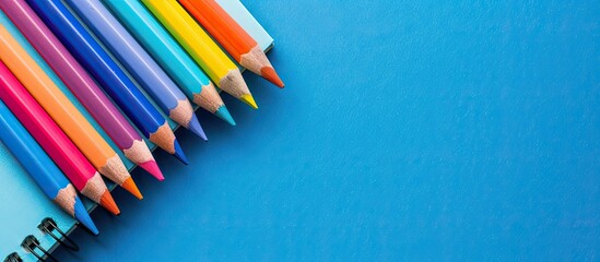 A blue background showcasing a notepad and colorful pencils from above suitable for various uses like business homeschooling or drawing with space for additional imagery