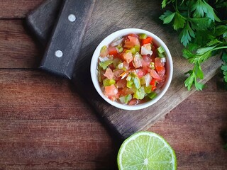 vinaigrette sauce tomatoes, peppers and onion in a white pot on a wooden background typical of a Brazilian barbecue