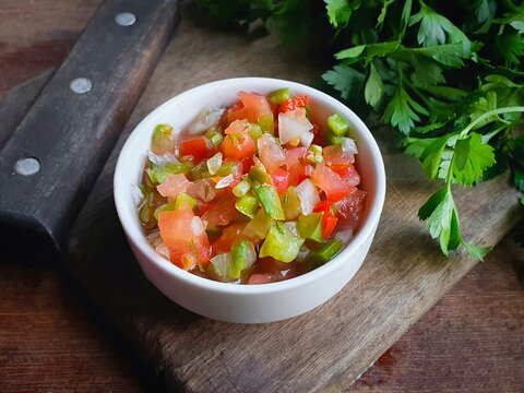vinaigrette sauce tomatoes, peppers and onion in a white pot on a wooden background typical of a Brazilian barbecue