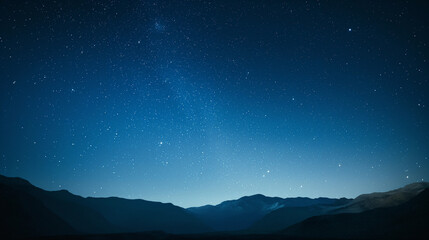 A clear night sky with a few stars and a mountain range in the background