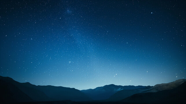 A clear night sky with a few stars and a mountain range in the background