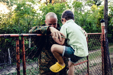 Naklejka premium Happy military father in uniform returning to family. An overjoyed boy is waiting to hug his dad who is returning after military service.