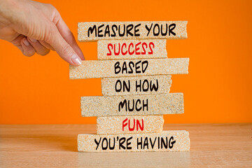 Motivational quote 'Measure your success based on how much fun you're having' on the brick blocks. Beautiful orange background, wooden table. Motivational concept.