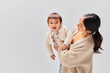 A young Asian mother tenderly holds her baby in her arms in a studio setting against a grey background.