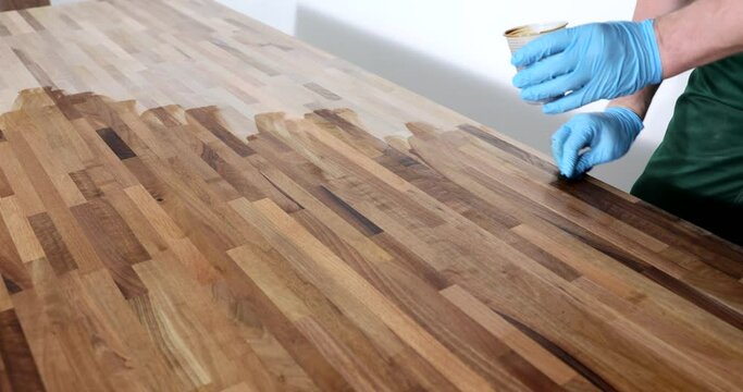 Foreman in rubber gloves processes parquet with varnish for smooth and glossy surface. Man polishes wood preparing for renovation slow motion