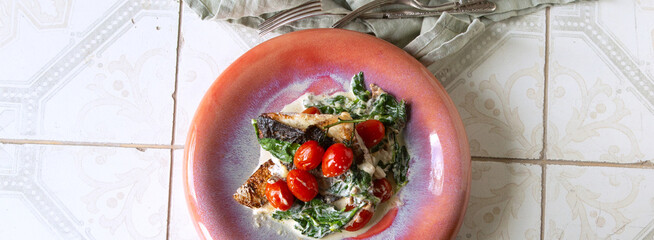 plate with fried sea bass with spinach and cherry tomatoes on the table