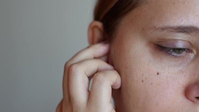 Close up of a young woman putting polyurethane earplugs in her ears with her hand on a dark grey background. Anti-noise earbuds for sleep, rest, travel, airplane