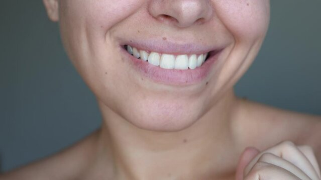 Gum health. Cropped shot of a young woman showing strong healthy teeth by tapping her finger on the enamel on a dark gray background. Dental care, dentistry concept