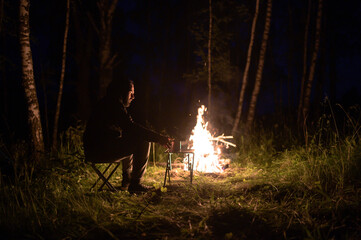 A man sits at night by a campfire in summer.