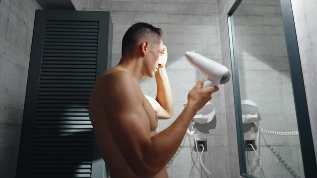 A worried young white man looks at himself in the mirror and inspects his premature receding hairline. Attractive Caucasian male adult in his 20s concerned about losing hair. Male pattern baldness. 
