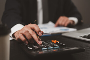 Businessman using calculator, reviewing financial documents. Focus on precise calculations, professional setting. Office environment, corporate finance. Financial planning, business strategy.