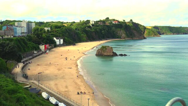 Tenby, Pembrokeshire, Wales: July 3rd 2024: 4K video, footage of families enjoying the evening sunshine on the golden sands of Tenby's north beach. The tide is up and water warm enough for paddling.