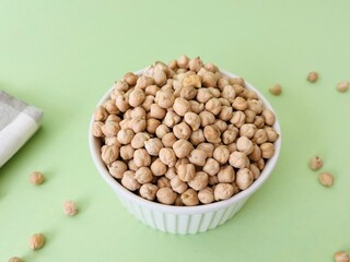 Raw dry chickpea in small ceramic bowl on green background. Traditional ingredient for cooking hummus. Middle Eastern and Mediterranean cuisine. Selected focused