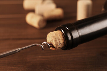 Wine bottle with corkscrew on wooden table, closeup