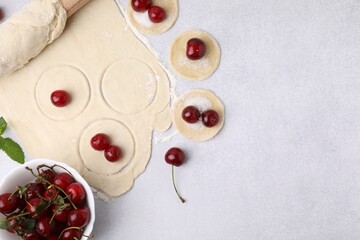 Process of making dumplings (varenyky) with cherries. Raw dough and ingredients on light table, flat lay. Space for text