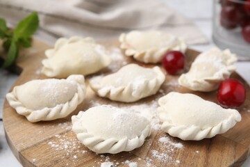 Raw dumplings (varenyky) and fresh cherries on table, closeup