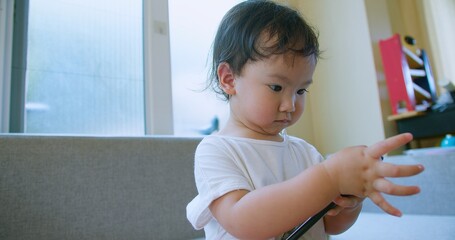 Adorable toddler child Playing engrossed in a smartphone while sitting on a sofa in a bright, modern living room.