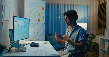 Young Asia male use laptop talk to colleague plan in video call meeting on desk in living room at home office overtime night. Work from house, financial plan, digital nomad job and Gen Z talent.