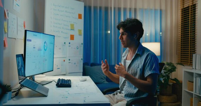 Young Asia male use laptop talk to colleague plan in video call meeting on desk in living room at home office overtime night. Work from house, financial plan, digital nomad job and Gen Z talent.