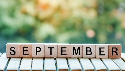 Wooden cubes with text SEPTEMBER on wooden table, natural green backdrop. Autumn season.