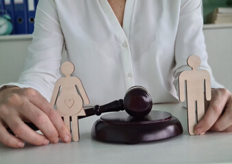 Wooden Figures Of A Pregnant Woman And Man Placed In Front Of A Judge's Gavel On A Desk