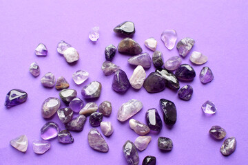 Small natural amethyst stones scattered on a purple background.