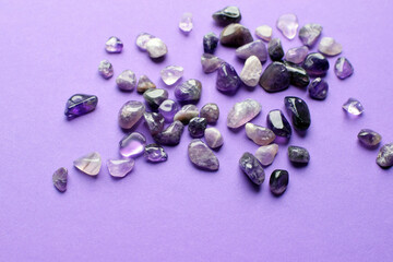 Small natural amethyst stones scattered on a purple background.