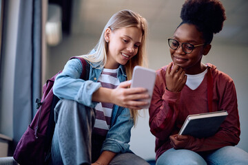 Happy university students using smart phone in lecture hall.