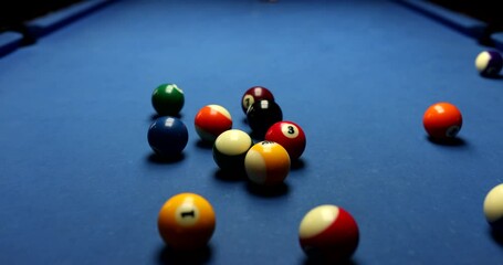 Focused player with cue aims at pyramid of colorful balls with digits. Man enjoys playing billiard on blue pool table in club slow motion - Powered by Adobe