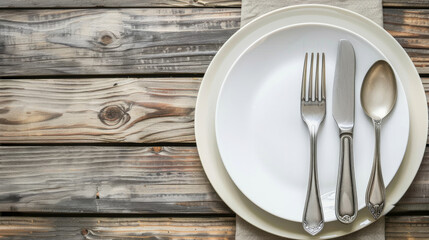 A neatly arranged flat lay of white plates and silver cutlery on a rustic wooden table creates a simple, clean dining setup.