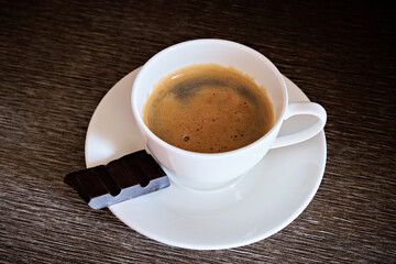 A cup of hot black coffee and chocolate on a dark wooden background. Selective focus