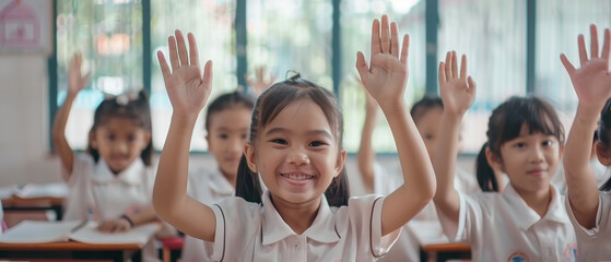 Smiling children in a classroom raise their hands enthusiastically, representing active participation and joy in learning.