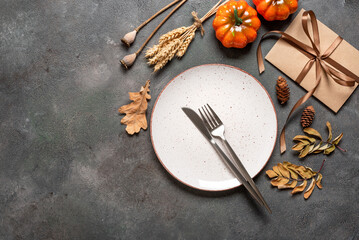 Autumn Thanksgiving table setting. White plate, cutlery, envelope tied with ribbon, decorative pumpkins and dried plants. Dark grunge background. Top view, flat lay.