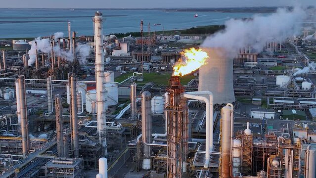 Aerial view of a chemical plant at sunset. Drone shot. Curling fire and cumin smoke filling the sky. Smoking chimneys from the factory. Chimneys of an oil refinery at sunrise pollute the environment