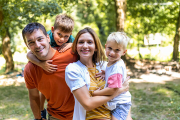 Fototapeta premium Family of four bonding in the park. Mother and father hugging with their sons.