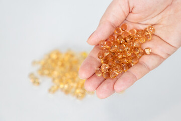 Fototapeta premium Hand holding a bunch of vitamin D gel capsules, with capsules blurred in a white background